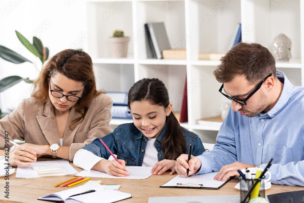 happy child drawing near parents in glasses working in office happy child drawing near parents in glasses working in office