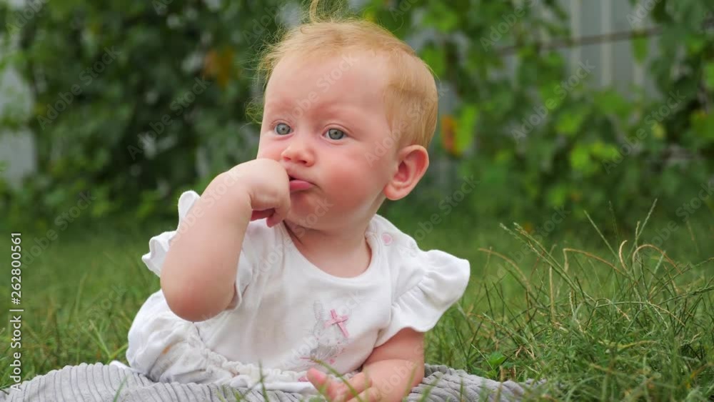 Baby teething background. Baby teething problems. Baby lying on green grass. Kid playing in the garden. Teeth are cutting through. Blue eyed girl smiling outdoor. Child in summer forest. Eco living. Baby teething background. Baby teething problems. Baby lying on green grass. Kid playing in the garden. Teeth are cutting through. Blue eyed girl smiling outdoor. Child in summer forest. Eco living.