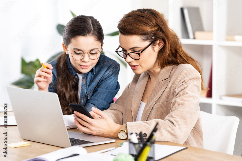 cute kid looking at smartphone near attractive mother in glasses cute kid looking at smartphone near attractive mother in glasses