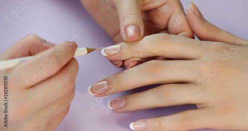 the manicurist paints the client s nails with white nail polish on a purple background  Painting nails. French manicure.