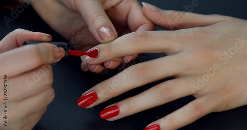 the manicurist paints the client s nails with red nail polish on a black background  Painting nails.