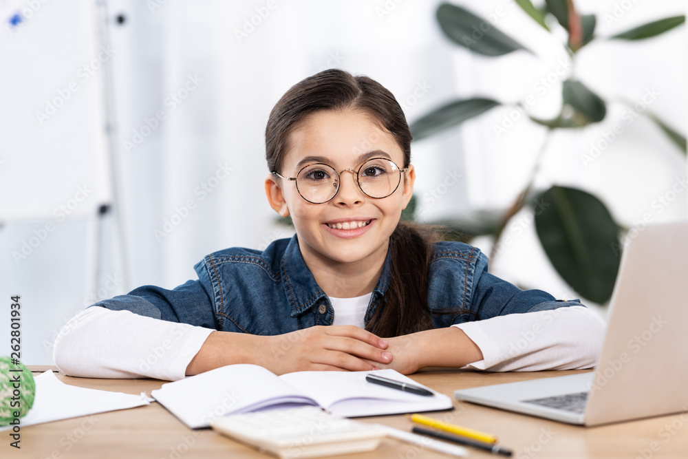 cheerful cute kid looking at camera near laptop in office cheerful cute kid looking at camera near laptop in office