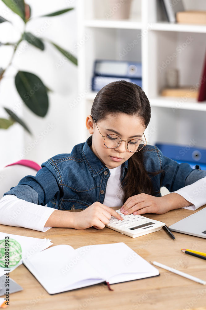 cute child in glasses using calculator while sitting in office cute child in glasses using calculator while sitting in office