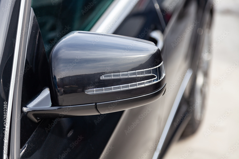 Black car front side mirror view with dark gray interior in excellent condition in a parking space among other cars