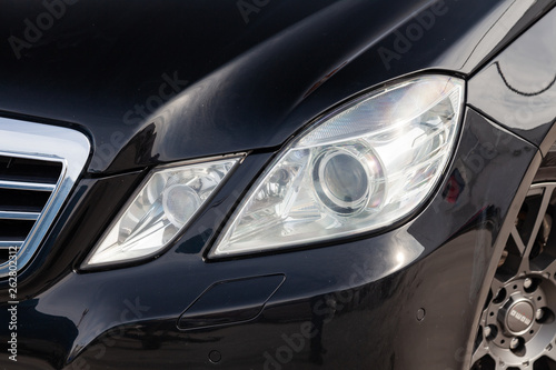 Black car front double headlight view with dark gray interior in excellent condition in a parking space among other cars