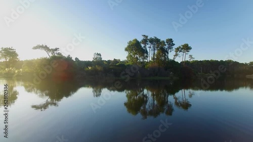 Aerial shot: flying through trees onto relective lake past a swing at sunset photo