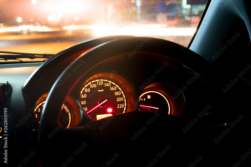 Speed meter of sport car inside at night, with light of car and city on the road.