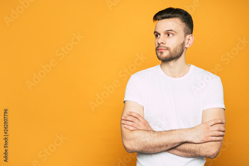 Stunning boy in casual outfit from sideway with a beard, thick shiny hair and big dark brown eyes next to the orange wall