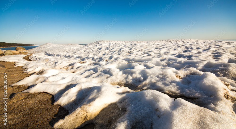 Fototapeta premium Snow pile, hill. Large snow drift isolated on a blue sky background, outdoor view of ice blocks at frozen finland lake in winter