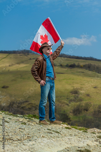 A man in a cowboy hat and a leather jacket in the mountains take canadian flag.