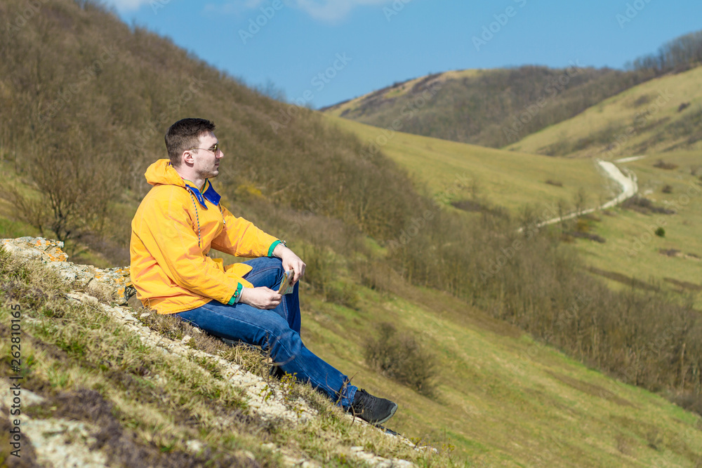 A tourist in a yellow jacket sits and looks at the mountains. Travel concept. A tourist in a yellow jacket sits and looks at the mountains. Travel concept.