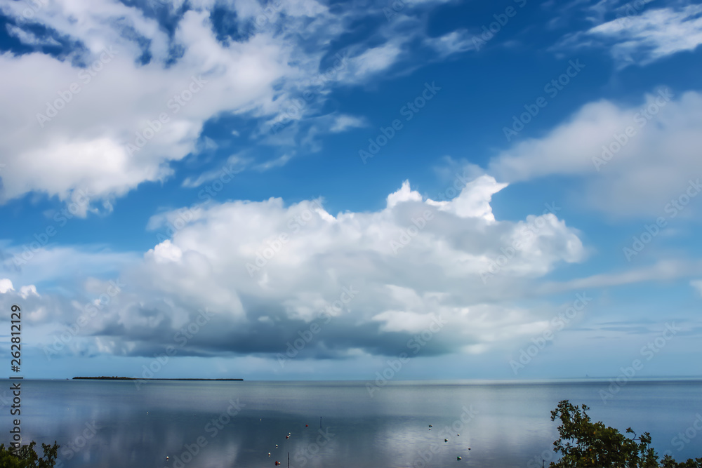 Fluffy cloudscape over the ocean still and calm reflecting the sky with an island in the distance