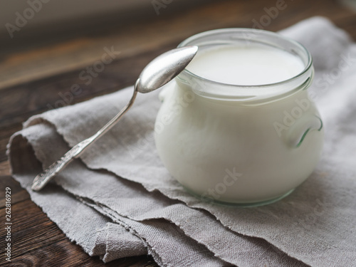 Natural homemade yogurt in a glass jar. Healthy food for breakfast. Linen tablecloth and silver spoon on on wooden table. photo