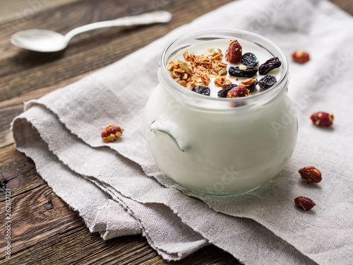 Natural homemade yogurt in a glass jar. Healthy food for breakfast with muesli. Jar with granola and banana sliceson linen tablecloth on on wooden table. photo