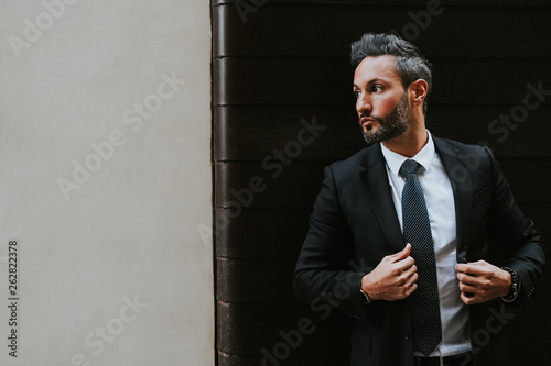 Adult handsome elegant businessman in formal suit looking away near wall photo