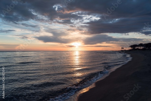 Sunset on the beach with a cloudy sky  calm sea and islands in the background