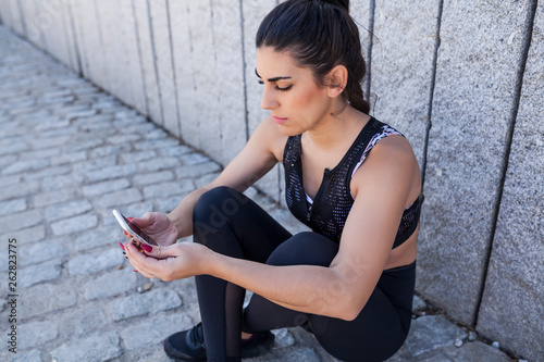 beautiful and brunette woman sit down and looking at the statistics of the training app photo