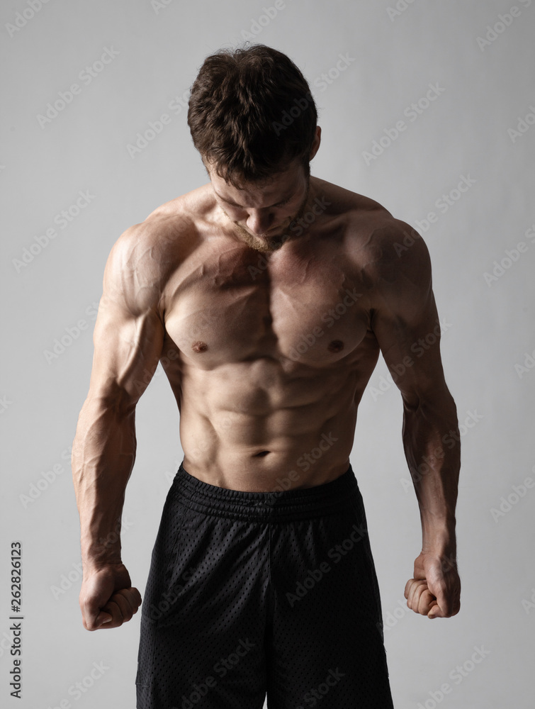 A very tense man with a naked torso in black shorts looks down on a gray background
