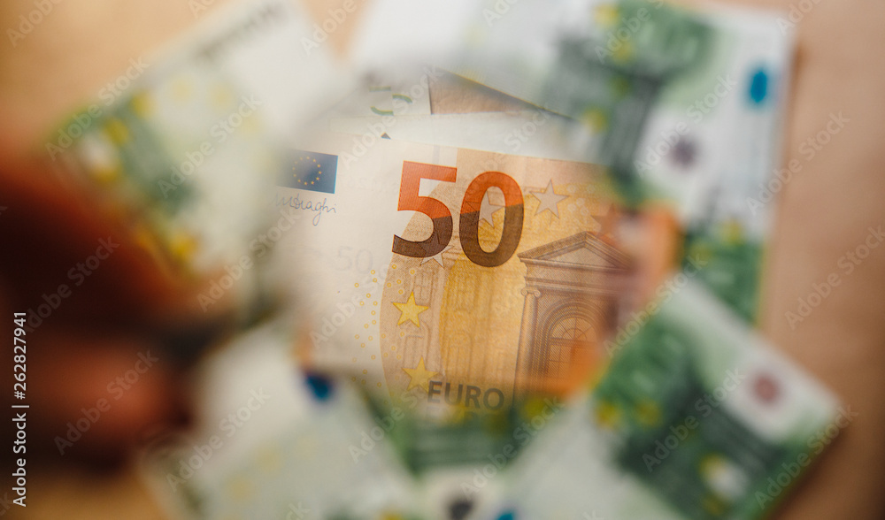 Checking a 50,100 euro banknote with a magnifying glass
