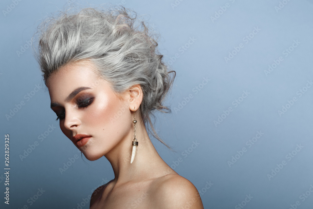 Profile portrait of fashionable, gorgeous young blonde woman, with amazing make up, naked shoulders, isolated on a blue background, copy space