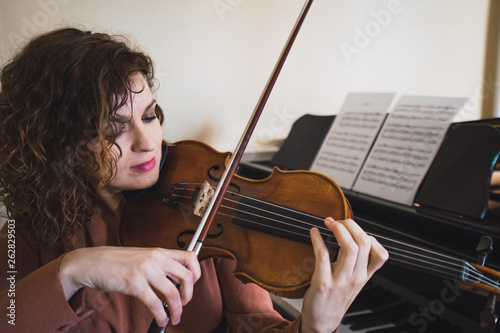 Woman sitting next to a piano playing a violin photo