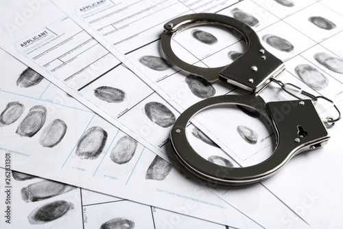 Fototapeta Handcuffs and fingerprint record sheets, closeup