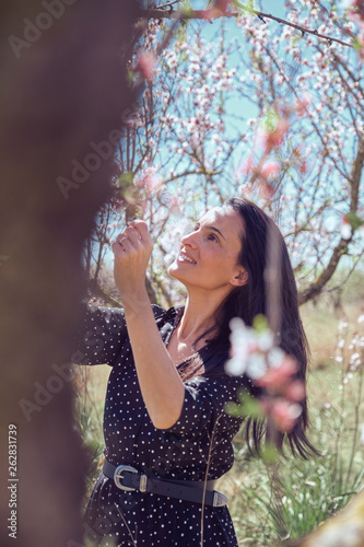 Young cheerful woman in dress near wood with amazing white and pink blooms on branches