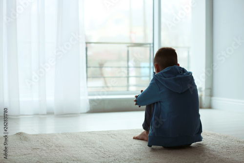 Upset boy sitting near window indoors. Space for text © New Africa