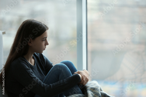 Upset teenage girl sitting at window indoors. Space for text Free Download Upset teenage girl sitting at window indoors. Space for text - GFXLoad