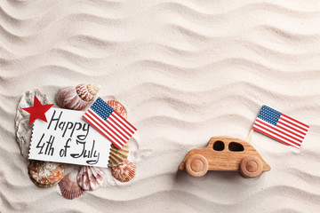 Flat lay composition with greeting card, USA flags and wooden car on sand. Happy Independence Day