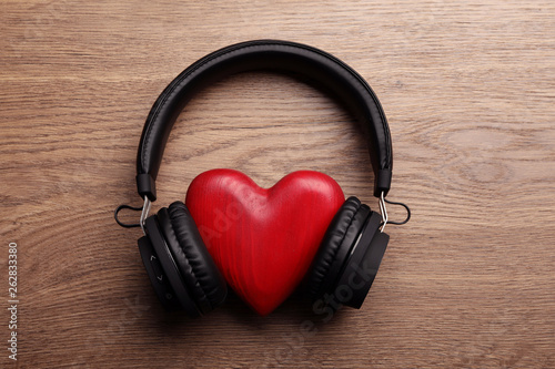 Decorative heart with modern headphones on wooden background, top view