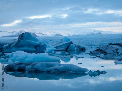 Beautiful glacier lagoon. Thousands of icebergs drifting lazily towards the sea, shining in many shades of blue. Soft sunset in the back. Thick clouds above the lagoon. Glacier's cap in the back