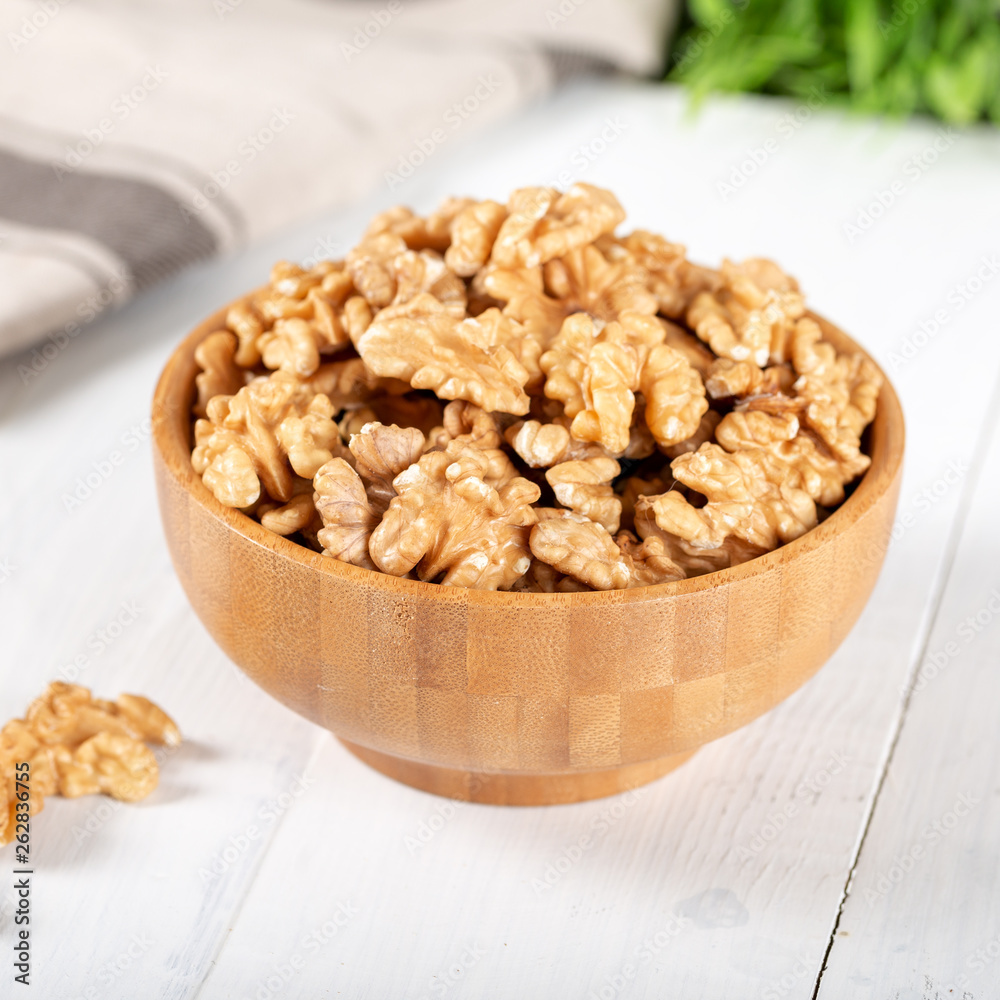 Walnut kernels in a wooden bowl on white background.