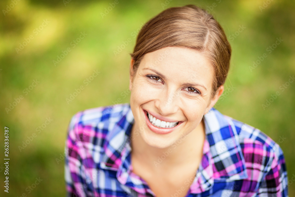 Closeup Of A woman smiling at the camera. At the park. Green background 