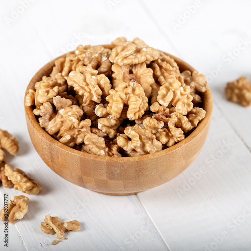 Walnut kernels in a wooden bowl on white background.