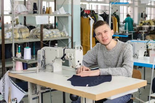 close up photo of a young man and other seamstresses sewing with sewing machine in a factory