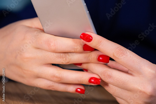 close-up, female hands with red manicure use a smartphone on a white background. Limited depth of field
