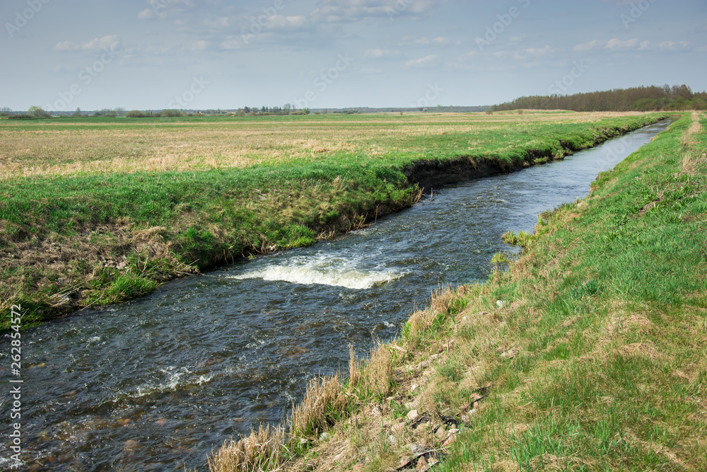 Wild river Uherka flowing through fields in eastern Poland and blue sky