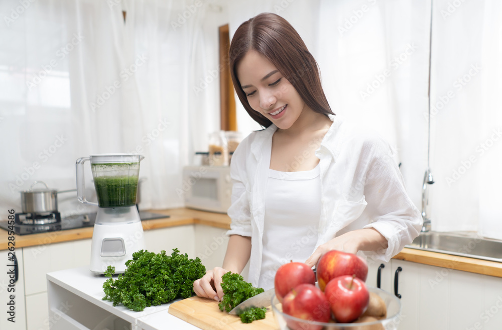 Happy Asian woman preparing healthy green vegetables in blender in her minimalist kitchen. Vegetarian, Healthy clean eating lifestyle concept