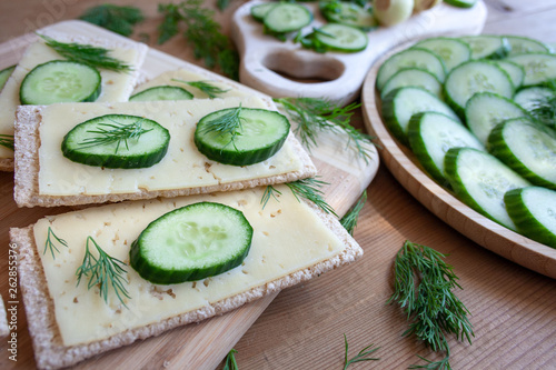 Light, spring sandwiches with cheese, fresh cucumber and dill, next to a tray with slices of cucumber and a board full of green spring vegetables