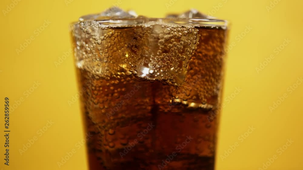 Glass full of cola fizzy drink with ice cubes. Cold coke sparkling soda on yellow background, moving bubbles slow motion Glass full of cola fizzy drink with ice cubes. Cold coke sparkling soda on yellow background, moving bubbles slow motion