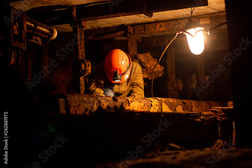 A young guy in a protective suit and helmet sits in a tunnel with a burning scrapbook. Miner in mine