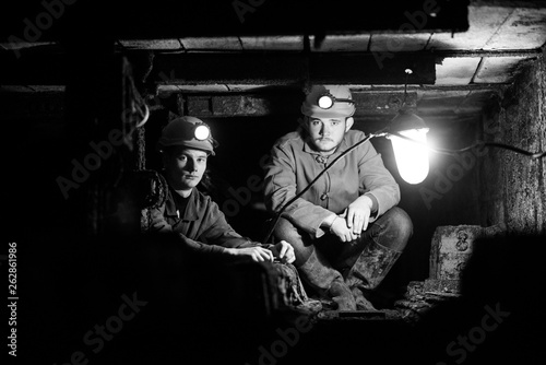 Two young guys in a protective suit and helmet are sitting in a tunnel with a burning scrap of paper. Miners in the mine