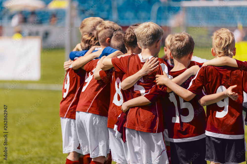 Fototapeta Soccer team huddling. Kids in red sportswear standing together and listening to coach. Junior football soccer tournament match