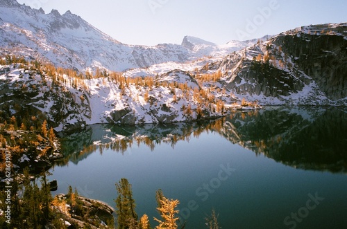 Mountain lake with reflection of snow and larch trees © Jeff Marsh/Stocksy