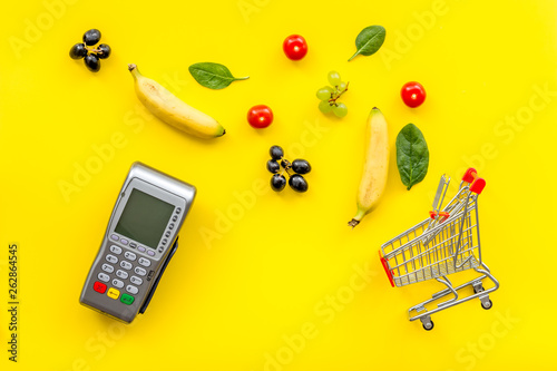 Online shopping concept with trolley, card machine near producs on yellow background top view photo