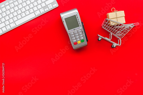 Online shopping concept with trolley near card machine, keyboard on red background top view copyspace