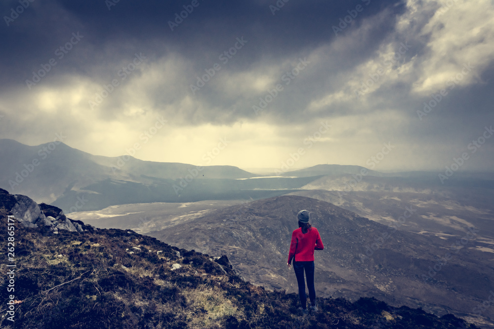 une femme en haut d'une montagne devant un paysage grandioses  sous un ciel menaçant, tons froids