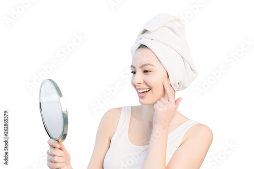 Quadro su tela portrait of attractive caucasian smiling woman on white studio shot cleaning her face looking at the mirror applying Foundation On Facial Skin