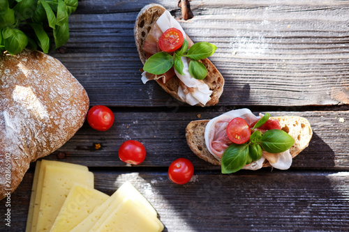 Small sandwiches with meat, cherry tomatoes, cheese, bread and basil on the black table.